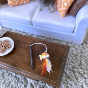 May include: A brown wooden table with a white plate of cookies and a toy fishing rod with a yellow and orange fish and feathers.