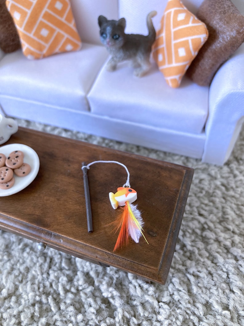 May include: A brown wooden table with a white plate of cookies and a toy fishing rod with a yellow and orange fish and feathers.