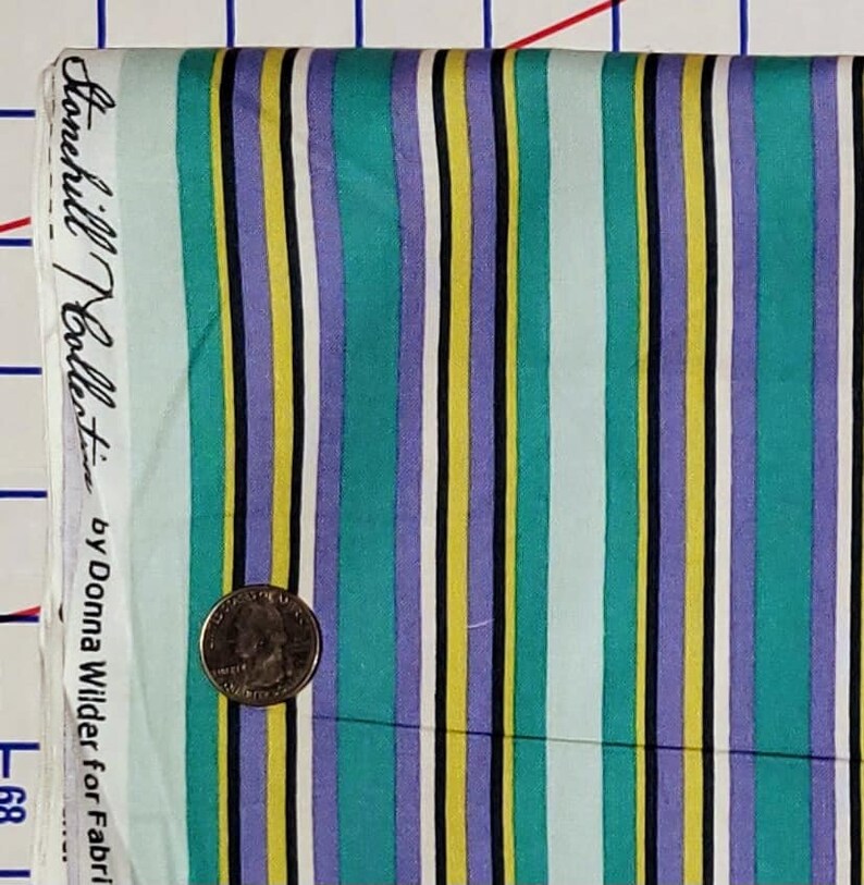 May include: Striped fabric with a teal, purple, yellow, and white color scheme. The fabric has a label that reads "Hanchilli Collection by Donna Wilder for Fabri"