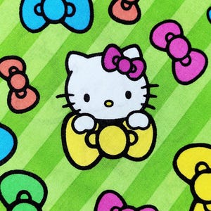 May include: A fabric pattern featuring the cartoon character Hello Kitty, with a white face, pink bow, and yellow outfit. The design includes colorful bows and is set against a green and white striped background.