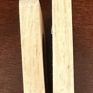 May include: Two wooden pieces of a puzzle, each with a light brown color and a wood grain pattern. The pieces are placed side by side, with a small gap between them.