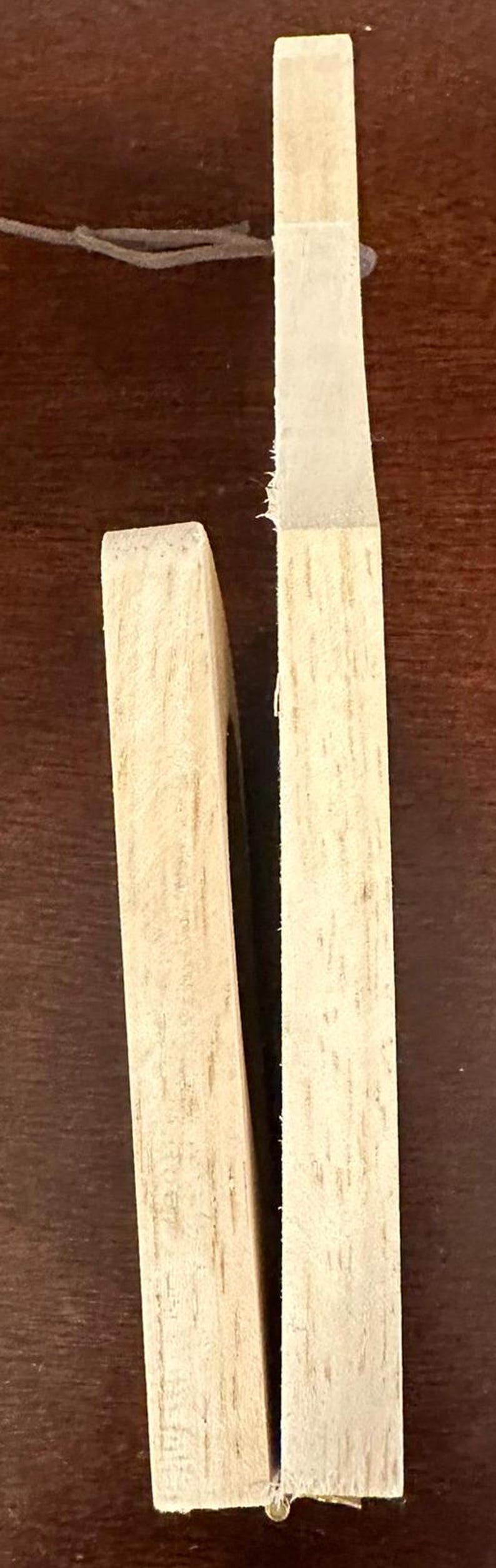 May include: Two wooden pieces of a puzzle, each with a light brown color and a wood grain pattern. The pieces are placed side by side, with a small gap between them.