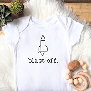 May include: White baby onesie with a black rocket ship graphic and the text "blast off."