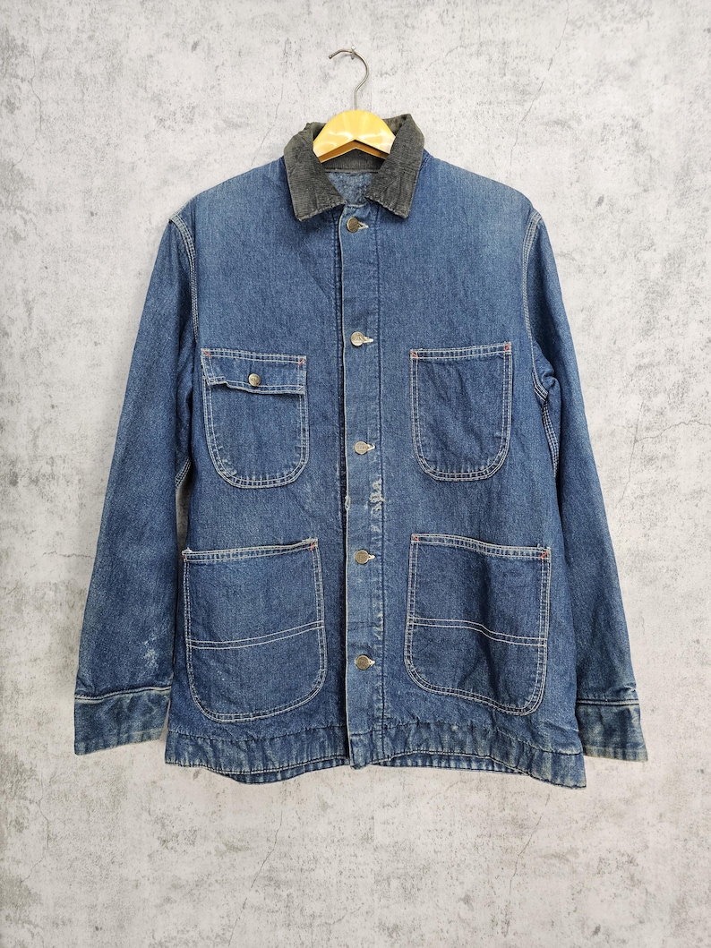 Puede incluir: Una chaqueta vaquera azul con cuello de pana. La chaqueta tiene varios bolsillos y cierre de botones.