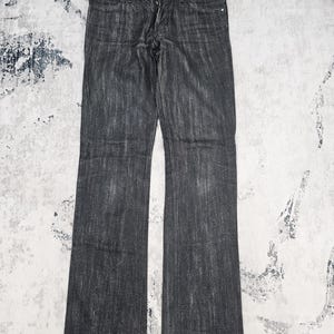 Könnte beinhalten: Eine dunkel anthrazitfarbene Jeans aus Denim mit geradem Bein, Knopfleiste und silberfarbenen Metallnieten an den Vordertaschen. Der Stoff weist ein dezentes vertikales Waschmuster auf, das sich über die gesamte Länge der Beine erstreckt.