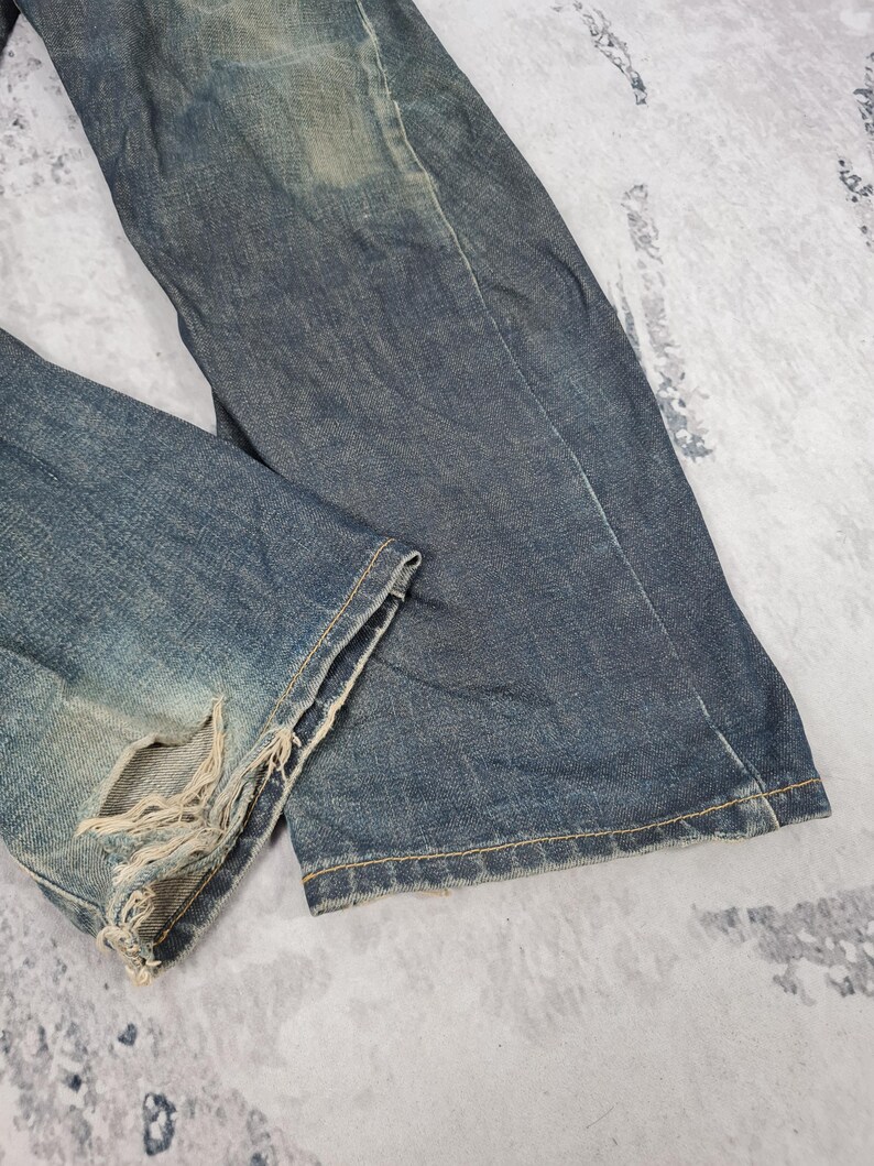 Op de afbeelding: Een paar blauwe denim jeans met distressed details en rafelige randen. De jeans heeft een vervaagde en versleten look, wat hem een vintage uitstraling geeft.