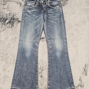 May include: A pair of blue denim jeans featuring a distressed wash with whiskering at the hips and thighs. The jeans have a classic five-pocket design, a button fly closure, and a slight flare at the leg openings with visible contrast stitching.