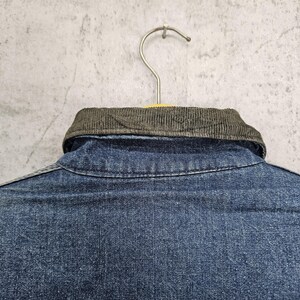 Puede incluir: Una camisa vaquera azul con cuello de pana. La camisa est&aacute; colgada en una percha.