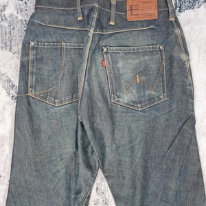 Op de afbeelding: Een paar donkerblauwe spijkerbroeken met een bruin leren patch op de achterkant van de tailleband met de tekst "Function Denim".