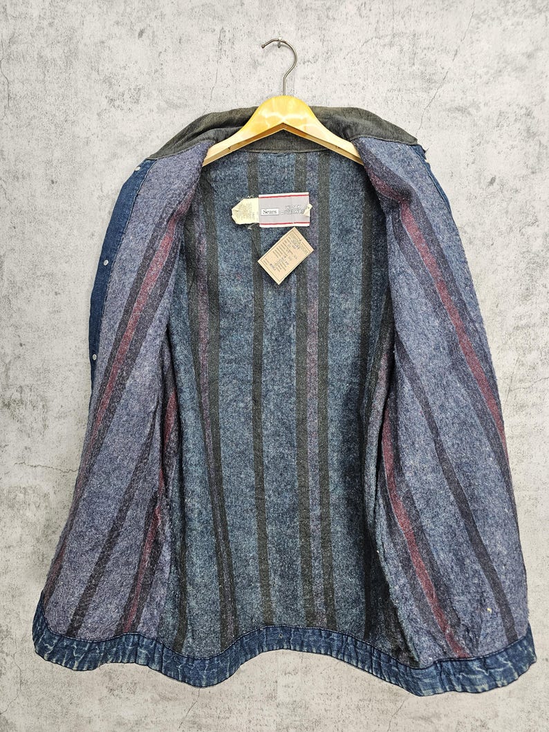 Puede incluir: Una chaqueta vaquera azul con forro de franela a rayas. La chaqueta tiene cierre de botones y dos bolsillos en la parte delantera. La etiqueta en el interior de la chaqueta dice "Scentsy".