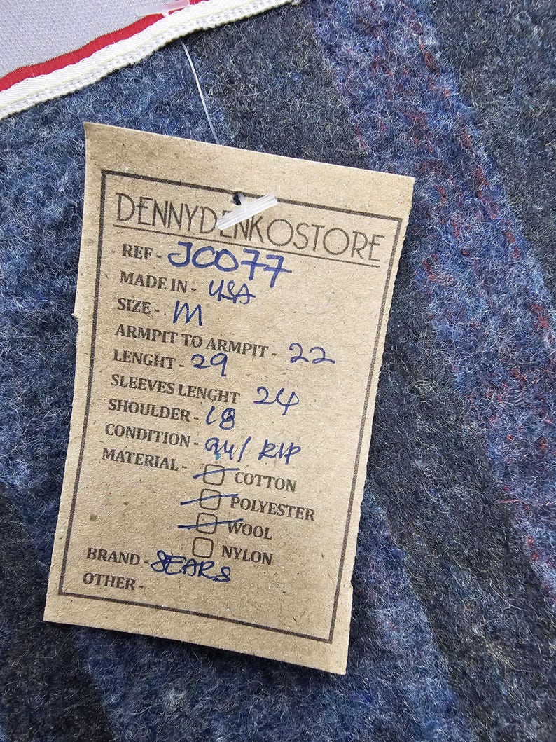 Puede incluir: Una etiqueta de papel marr&oacute;n con texto negro que detalla el tama&ntilde;o, las medidas y el material de una prenda. La etiqueta dice "DENNYDENKOSTORE", "REF-J0077", "MADE IN USA", "SIZE-M", "ARMPIT TO ARMPIT-22", "LENGHT-29", "SLEEVES LENGHT 24", "SHOULDER-18", "CONDITION-au/ RIP", "MATERIAL-COTTON", "POLYESTER", "WOOL", "NYLON", "BRAND-SEARS", "OTHER-".