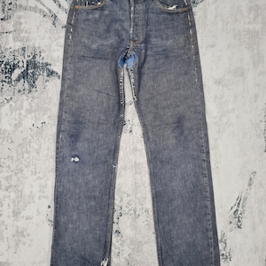 May include: A pair of blue denim jeans with distressed details and a small tear on the front. The jeans have a straight leg and a classic five-pocket style.