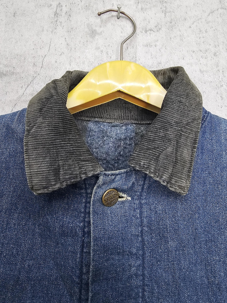 Puede incluir: Una chaqueta vaquera azul con cuello de pana. La chaqueta tiene cierre de botones y un solo bot&oacute;n en el pecho.