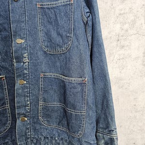 Puede incluir: Una chaqueta vaquera azul con m&uacute;ltiples bolsillos y cierres de bot&oacute;n. La chaqueta tiene un aspecto desgastado y est&aacute; hecha de una tela gruesa y duradera.