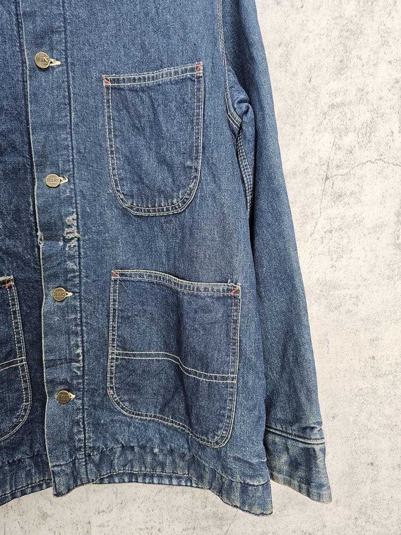 Puede incluir: Una chaqueta vaquera azul con m&uacute;ltiples bolsillos y cierres de bot&oacute;n. La chaqueta tiene un aspecto desgastado y est&aacute; hecha de una tela gruesa y duradera.