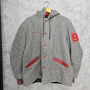 Peut inclure: Une veste de baseball à capuche grise avec des bordures rouges et un écusson en feutre rouge avec le numéro 8 sur la manche droite. La veste a une fermeture à boutons et deux poches. Le mot "Tracy" est brodé sur la poitrine gauche.