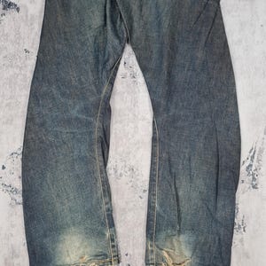 Op de afbeelding: Een paar blauwe denim jeans met distressed details en rafelige zoom.