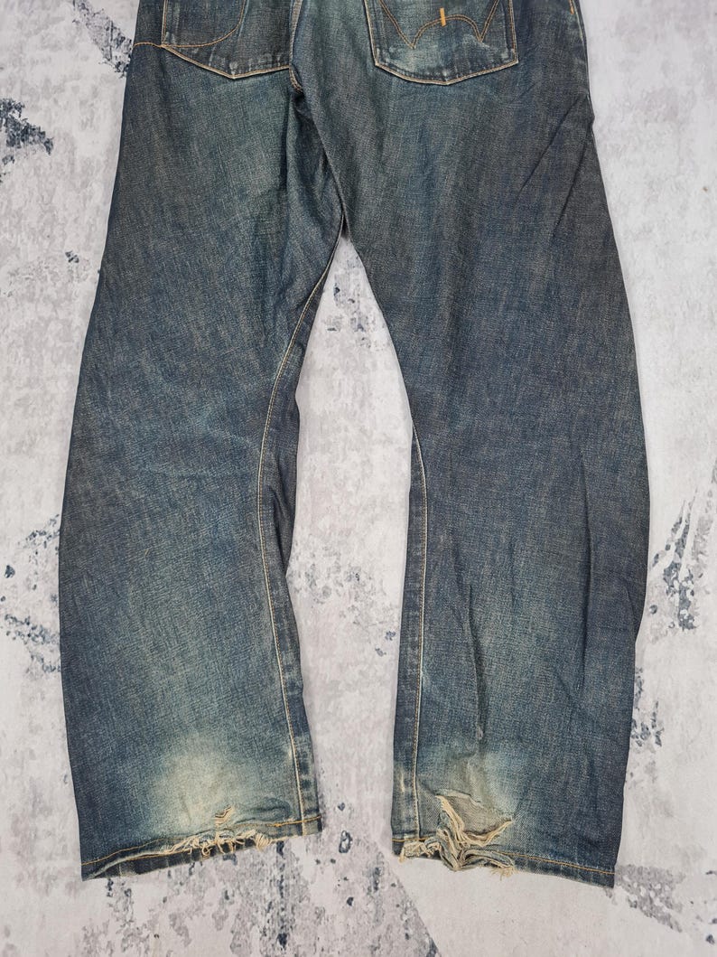 Op de afbeelding: Een paar blauwe denim jeans met distressed details en rafelige zoom.