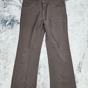 Puede incluir: Pantalones marrones con un diseño clásico. Los pantalones tienen cierre de botón y cremallera, bolsillos delanteros y una pernera acampanada. La tela parece ser de peso medio.