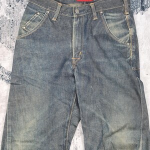 Op de afbeelding: Een donkerblauwe spijkerbroek met een rood "Evisu" label op de achterkant van de tailleband.