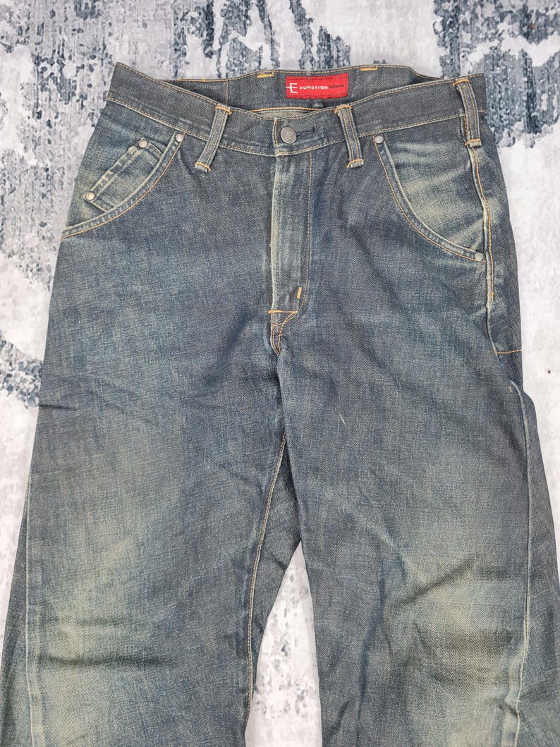 Op de afbeelding: Een donkerblauwe spijkerbroek met een rood "Evisu" label op de achterkant van de tailleband.