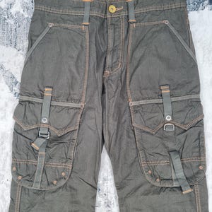 May include: Khaki-colored cargo pants with multiple pockets and orange stitching. The pants have a button closure and belt loops. The text "505 KHAKI" is visible on the waistband.