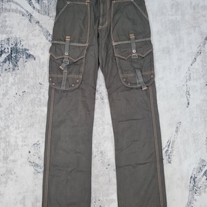 May include: Dark olive green cargo pants with multiple pockets and straps. The pants have visible orange stitching and the text "505 KHAKI" on the waistband. The pants are made of a durable fabric.