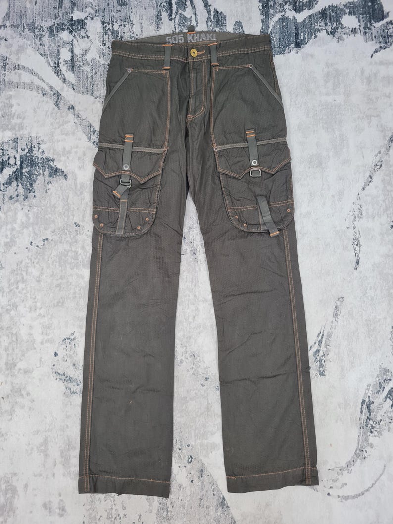 May include: Dark olive green cargo pants with multiple pockets and straps. The pants have visible orange stitching and the text "505 KHAKI" on the waistband. The pants are made of a durable fabric.