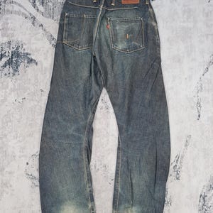 Op de afbeelding: Een paar blauwe denim jeans met distressed details en een rood leren patch op de achterkant van de tailleband. De jeans heeft een rechte pijp en een faded wash.