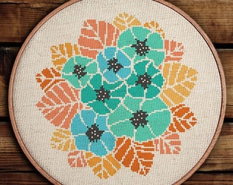 Puede incluir: Un bastidor de bordado circular de madera que contiene una pieza de tela Aida de color blanco roto. La tela presenta un patrón de punto de cruz de un ramo floral con pétalos y hojas de color verde azulado, azul claro, naranja y amarillo, con centros gris oscuro.
