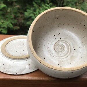 May include: A white ceramic bowl with a speckled glaze and a spiral design on the inside. The bowl has a matching plate.