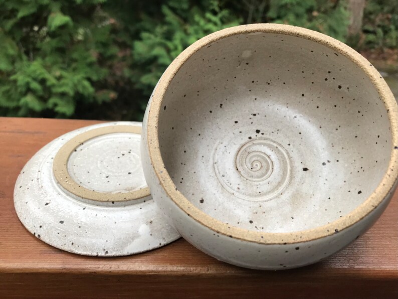 May include: A white ceramic bowl with a speckled glaze and a spiral design on the inside. The bowl has a matching plate.