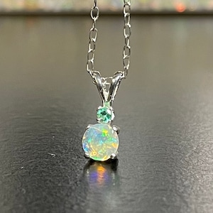 May include: A silver chain necklace with a pendant featuring a round, white opal gemstone with green accents.