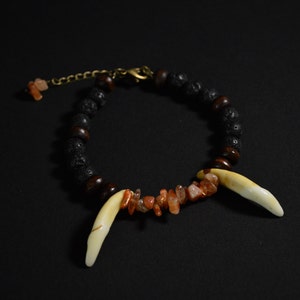 May include: A black lava rock and carnelian gemstone bracelet with two white tooth charms.