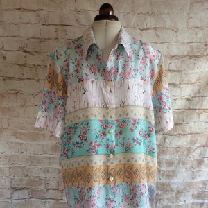 May include: A short-sleeved button-down shirt with a patchwork design. The shirt features alternating horizontal stripes of floral patterns, geometric shapes, and solid colours in pink, teal, and peach. The shirt is displayed on a mannequin.