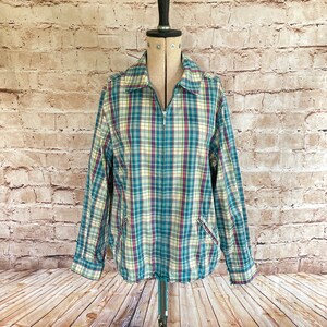 May include: A long-sleeve zip-up jacket featuring a plaid pattern in shades of teal, magenta, yellow, and white. The jacket includes a pointed collar, a full-length front zipper, two slanted zippered pockets at the waist, and a drawstring hem.