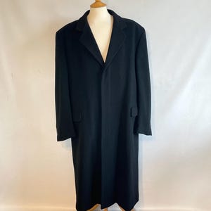 Puede incluir: Un abrigo largo de color negro sólido que presenta un cuello con solapa de muesca, mangas largas y dos bolsillos con solapa en la cintura. El abrigo se muestra en un maniquí, exhibiendo un diseño estructurado de cuerpo entero con cierre frontal.