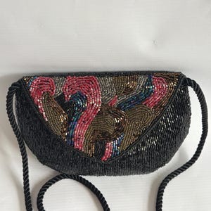 May include: Black beaded evening bag with a colourful beaded design on the flap. The flap features a pattern of red, brown, blue, and gold beads. The bag has a black rope strap.