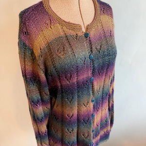 May include: A long-sleeved knit cardigan featuring a multi-colored gradient pattern of purple, blue, and gold tones. The garment includes a round neckline, a vertical button-down front with small blue buttons, and a repeating V-shaped eyelet stitch pattern throughout the fabric.