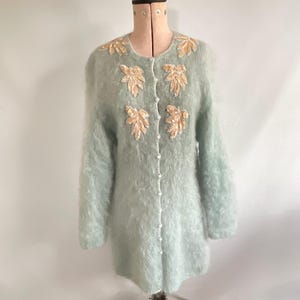 Puede incluir: Una taza de cerámica blanca con asa negra y el texto "But First, Coffee" en negro en negrita. La taza está sobre una superficie blanca.