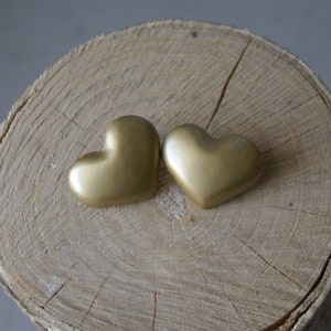 Op de afbeelding: Twee gouden hartvormige ornamenten op een houten oppervlak.