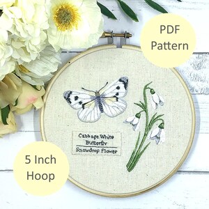 以下が含まれることがあります： 5インチのフープに、キャベツホワイトバタフライとスノードロップの花の刺繍デザイン。デザインには、「Cabbage White Butterfly Snowdrop Flower」というテキストが含まれています。