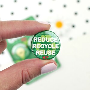 May include: Green button with white text that reads "Reduce Recycle Reuse". The button has a green leaf design around the edge and two red hearts at the bottom.