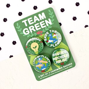 May include: A set of four green and white eco-friendly buttons with slogans like "Think Green", "Save the Planet", "I Love My Planet", and "Reduce Recycle Reuse". The buttons are on a green card with the words "Team Green" in white.