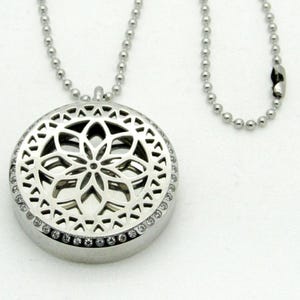 Peut inclure: Un collier en argent avec un pendentif rond orné d'un motif floral détaillé. Le pendentif est entouré d'une rangée de cristaux transparents.