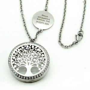May include: A silver-toned metal locket necklace featuring a circular pendant with a cut-out tree design and a border of small clear crystals. A round metal tag is attached to the chain, engraved with the text: Henson, 454 South Fork, American, Utah, (420)971-3506.
