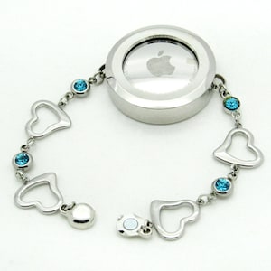 May include: A silver bracelet with a round charm featuring an Apple logo. The bracelet has a magnetic clasp and is decorated with blue crystal hearts.