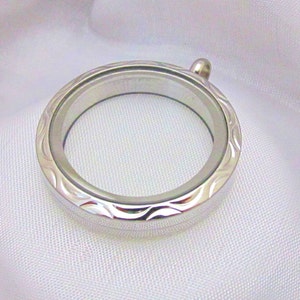 May include: A silver locket pendant with a wavy design around the edge. The locket is open and has a clear glass insert.
