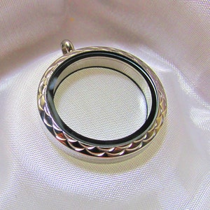 Peut inclure: Un pendentif de locket en argent avec un bord festonné et un insert en verre transparent. Le locket est conçu pour contenir une petite photo ou un autre souvenir.