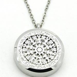 May include: A silver-colored pendant necklace with a detailed, openwork design. The pendant is round with a starburst pattern in the center and a decorative border. The chain is also silver and hangs from the pendant.